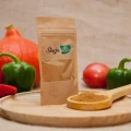 Cynamon cejloński mielony BIO w kraftowym opakowaniu Stacja Bio na drewnianej desce z drewnianą łyżką przyprawy i warzywami w tle – ekologiczna przyprawa o delikatnym aromacie.png