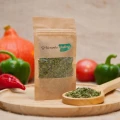Oregano suszone w kraftowym opakowaniu W Kierunku Natury na drewnianej desce z łyżką przyprawy i warzywami w tle.png
